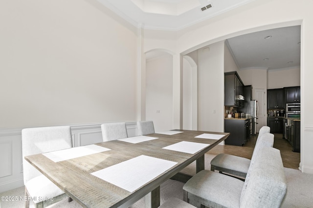 dining space with visible vents, arched walkways, a wainscoted wall, crown molding, and a decorative wall