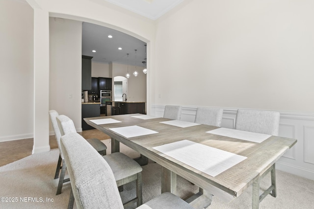 dining room featuring light carpet, wainscoting, arched walkways, and a decorative wall