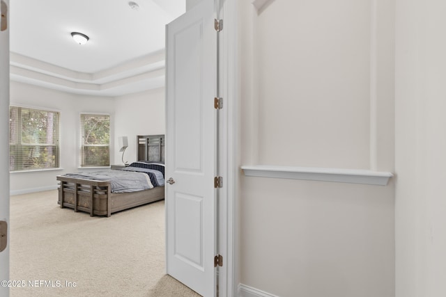 carpeted bedroom featuring a raised ceiling and baseboards