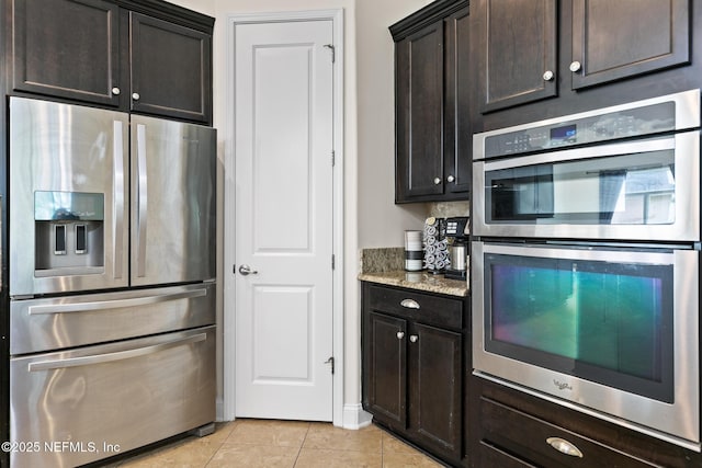 kitchen featuring light tile patterned floors, stainless steel appliances, dark brown cabinetry, and light stone countertops