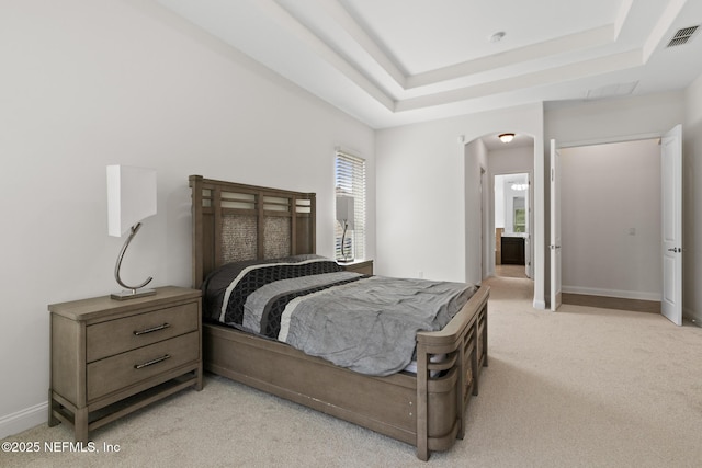 bedroom with a tray ceiling, arched walkways, visible vents, light carpet, and baseboards