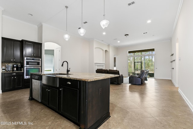 kitchen with a sink, visible vents, appliances with stainless steel finishes, an island with sink, and crown molding