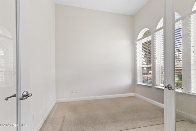 carpeted empty room featuring french doors and baseboards