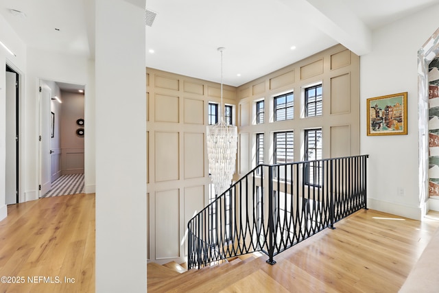 hall featuring visible vents, beamed ceiling, light wood-style flooring, and an upstairs landing