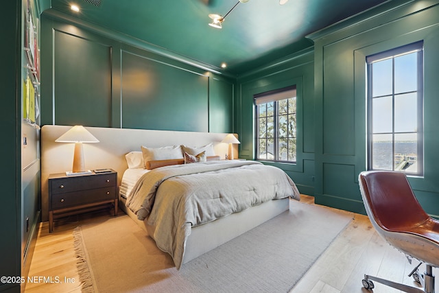 bedroom with crown molding, light wood-style flooring, and a decorative wall