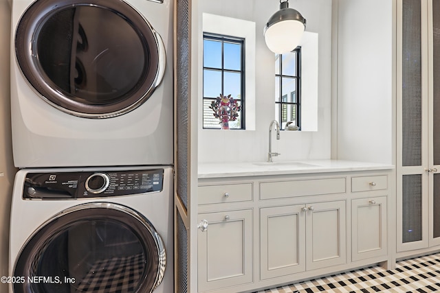 clothes washing area with stacked washer / dryer, cabinet space, and a sink