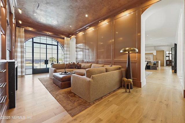 living room featuring light wood-style floors, arched walkways, crown molding, and a decorative wall