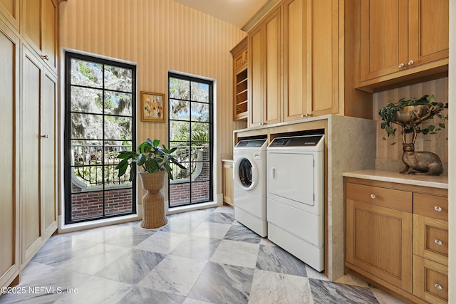 clothes washing area with cabinet space, washer and clothes dryer, and wallpapered walls