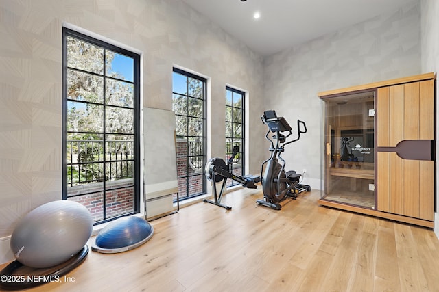 workout area with baseboards, light wood-style flooring, and a high ceiling