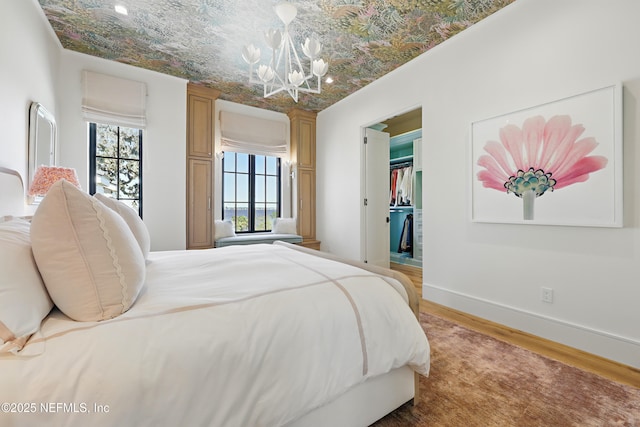 bedroom with wood finished floors, baseboards, a spacious closet, an ornate ceiling, and an inviting chandelier