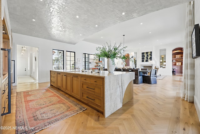 kitchen with light stone counters, recessed lighting, a large island with sink, and a sink