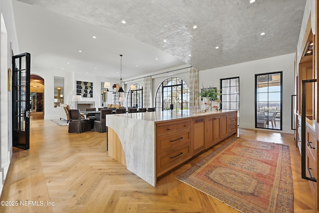 kitchen featuring baseboards, arched walkways, a spacious island, light stone counters, and recessed lighting