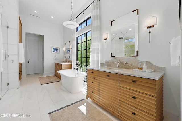 bathroom with a stall shower, a freestanding tub, two vanities, and a sink