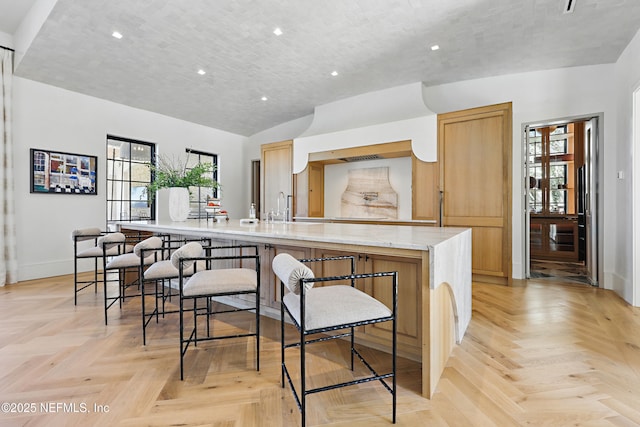 kitchen featuring a spacious island, a breakfast bar area, vaulted ceiling, and baseboards