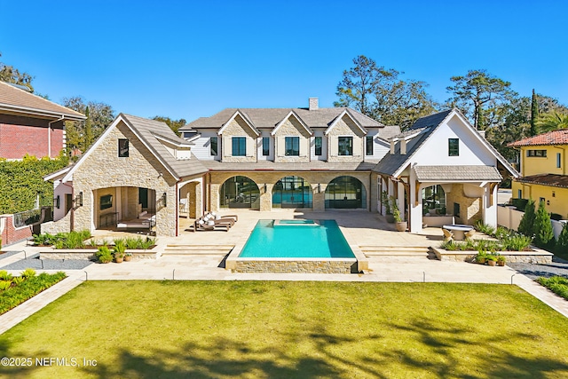 rear view of property with an outdoor pool, stone siding, fence, a yard, and a patio area