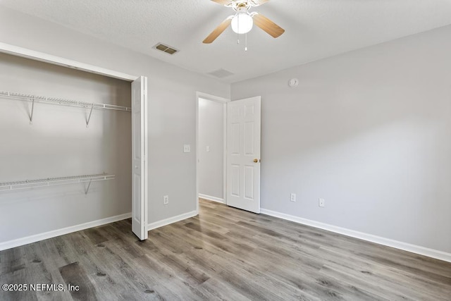 unfurnished bedroom featuring a textured ceiling, wood finished floors, visible vents, baseboards, and a closet