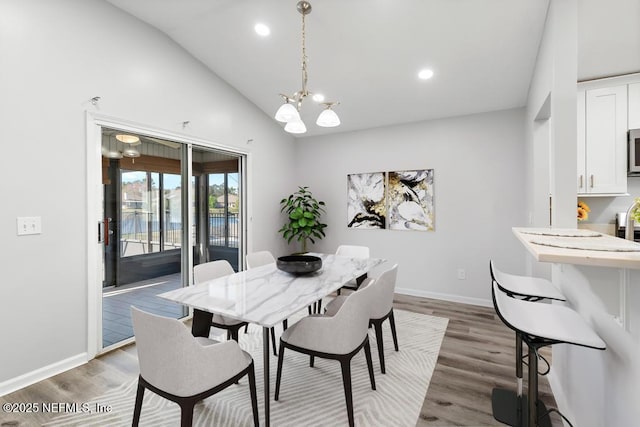 dining space featuring lofted ceiling, light wood finished floors, an inviting chandelier, and baseboards