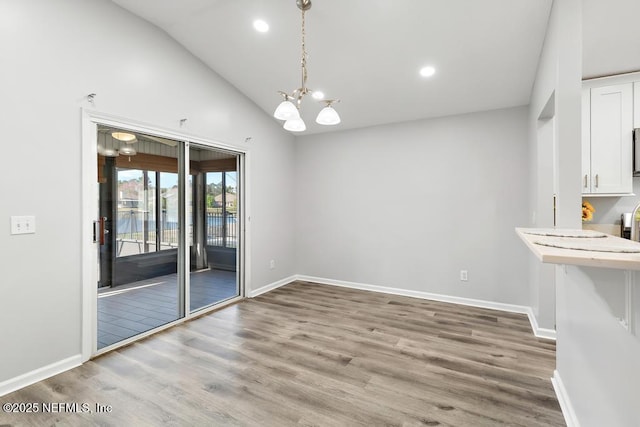 unfurnished dining area featuring baseboards, lofted ceiling, wood finished floors, an inviting chandelier, and recessed lighting