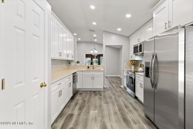 kitchen with light countertops, appliances with stainless steel finishes, white cabinetry, vaulted ceiling, and a sink