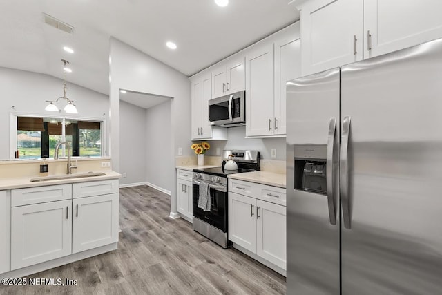 kitchen with appliances with stainless steel finishes, vaulted ceiling, white cabinetry, and a sink