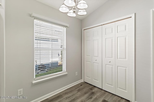 unfurnished bedroom featuring dark wood finished floors, a closet, an inviting chandelier, vaulted ceiling, and baseboards