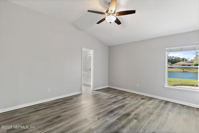 unfurnished room featuring baseboards, a ceiling fan, lofted ceiling, wood finished floors, and a water view