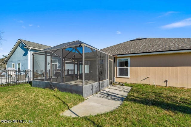 rear view of house featuring a shingled roof, glass enclosure, a yard, and fence