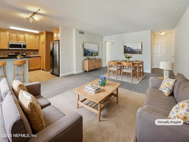 living area with visible vents, a textured ceiling, baseboards, and light tile patterned floors