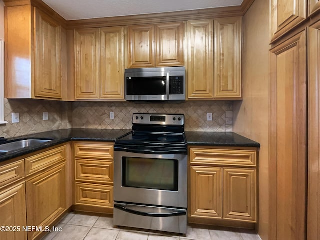 kitchen with dark stone counters, decorative backsplash, appliances with stainless steel finishes, a sink, and light tile patterned flooring