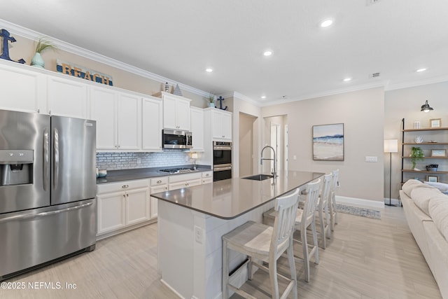 kitchen with backsplash, a center island with sink, a breakfast bar, stainless steel appliances, and a sink