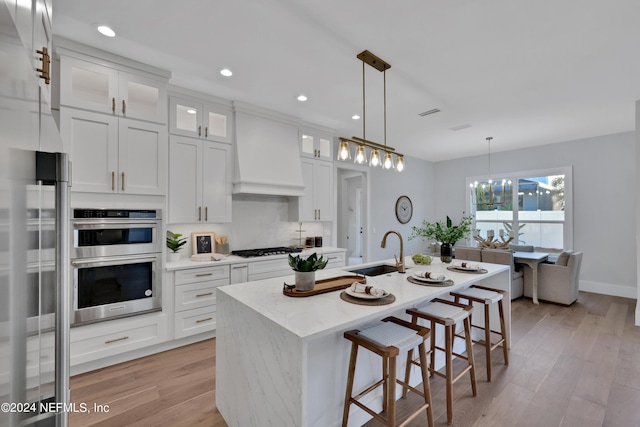 kitchen with light wood finished floors, premium range hood, double oven, and a sink