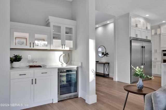 bar featuring wine cooler, recessed lighting, bar area, appliances with stainless steel finishes, and light wood finished floors