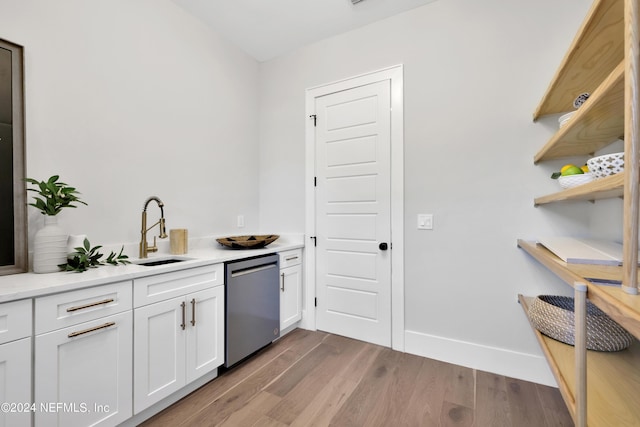 kitchen with wood finished floors, light countertops, stainless steel dishwasher, white cabinetry, and a sink