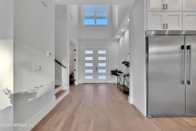 foyer entrance with visible vents, baseboards, a towering ceiling, stairs, and light wood-style floors