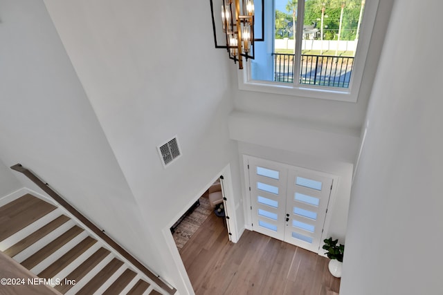 entrance foyer with a chandelier, a towering ceiling, wood finished floors, and visible vents