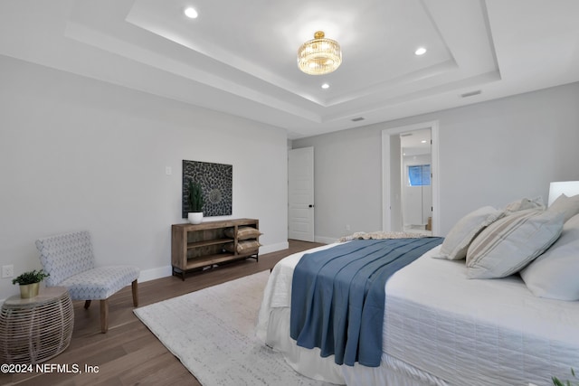 bedroom with a tray ceiling, recessed lighting, visible vents, wood finished floors, and baseboards