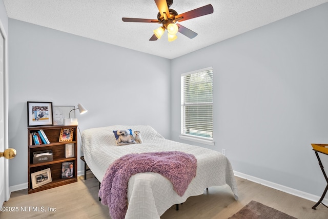 bedroom with light wood-style floors, a textured ceiling, baseboards, and a ceiling fan