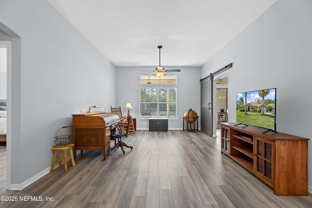 living area featuring a ceiling fan, a barn door, baseboards, and wood finished floors