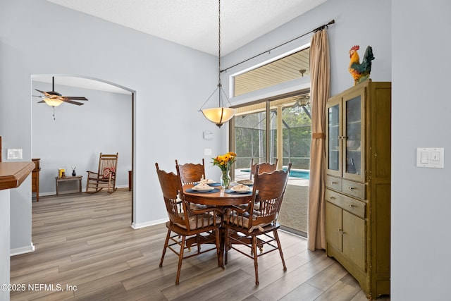 dining space featuring baseboards, arched walkways, a ceiling fan, light wood-style flooring, and a textured ceiling