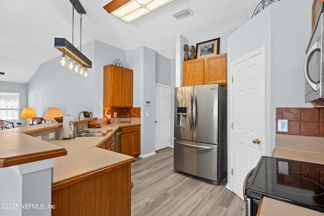 kitchen featuring visible vents, a peninsula, stainless steel appliances, light wood-type flooring, and a sink