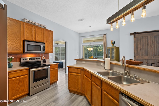 kitchen featuring a barn door, arched walkways, light wood-style flooring, stainless steel appliances, and a sink