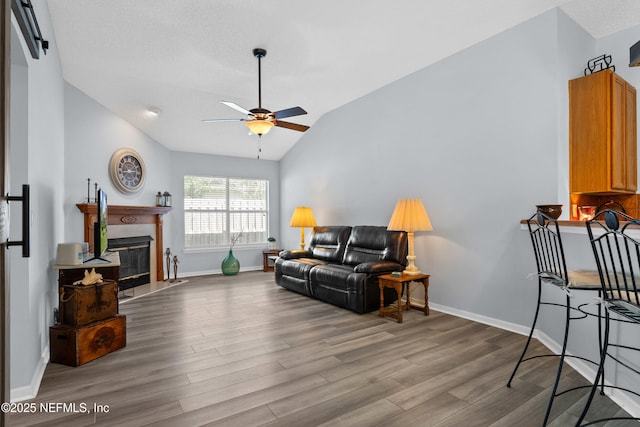 living area featuring lofted ceiling, a premium fireplace, wood finished floors, a ceiling fan, and baseboards