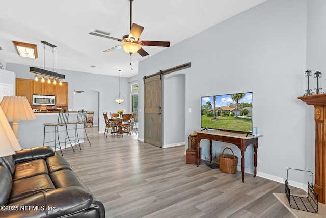 living room featuring visible vents, a barn door, a ceiling fan, light wood-style floors, and baseboards