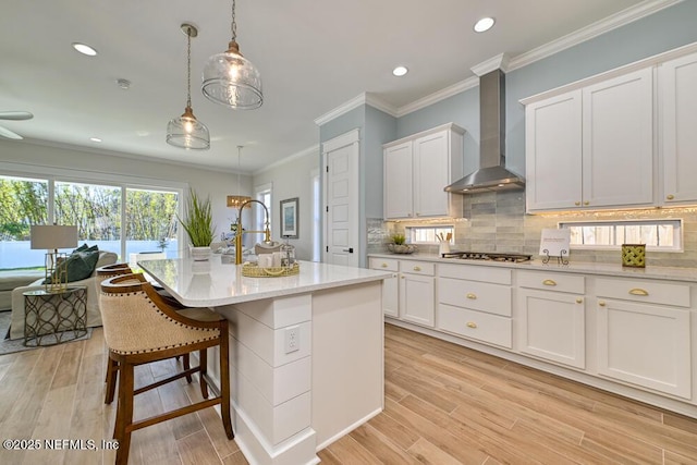 kitchen featuring stainless steel gas cooktop, crown molding, wall chimney exhaust hood, light wood-type flooring, and backsplash