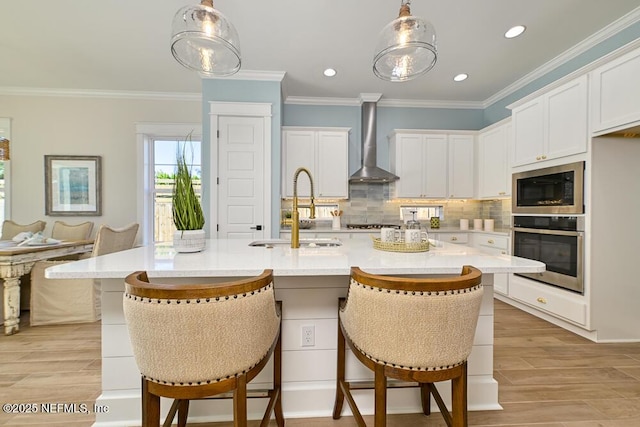 kitchen with light countertops, wall chimney exhaust hood, appliances with stainless steel finishes, and a sink