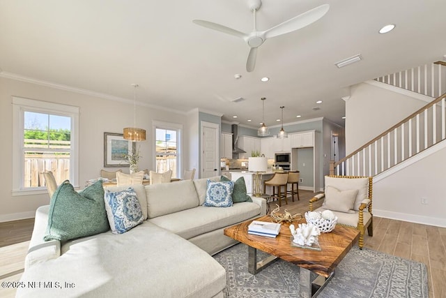 living area featuring stairway, baseboards, ornamental molding, and light wood finished floors