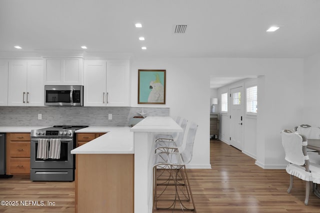 kitchen with visible vents, a peninsula, stainless steel appliances, a kitchen bar, and tasteful backsplash