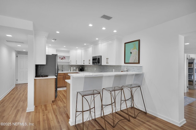 kitchen featuring open shelves, stainless steel microwave, backsplash, a peninsula, and light countertops