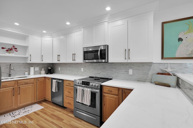 kitchen featuring light wood-style flooring, a sink, decorative backsplash, stainless steel appliances, and white cabinets