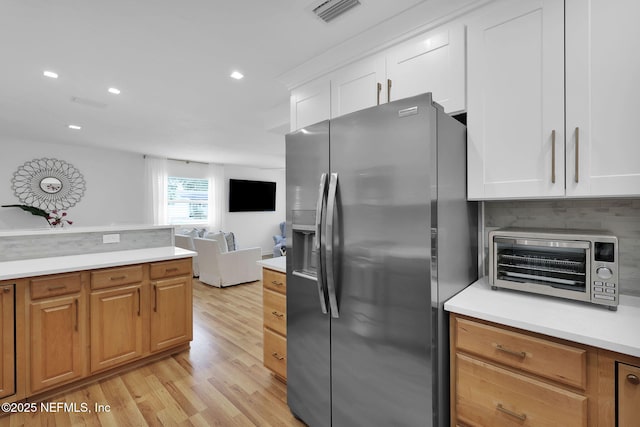 kitchen with a toaster, stainless steel fridge, white cabinetry, and light countertops